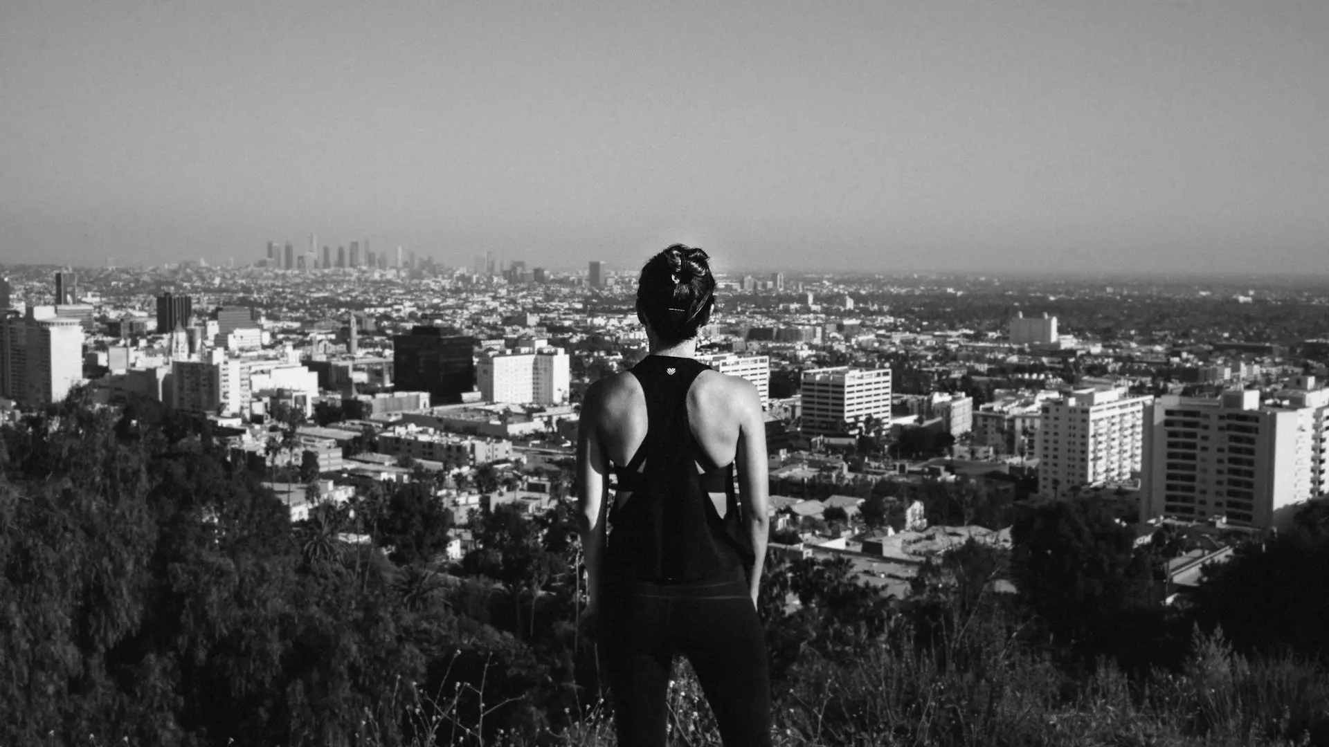 grayscale photography of woman standing near high buildings
